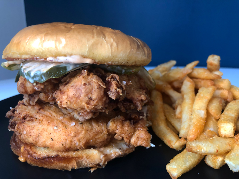 A giant fried chicken sandwich from Billy Barooz is on a black plate next to a pile of french fries. Photo by Alyssa Buckley.