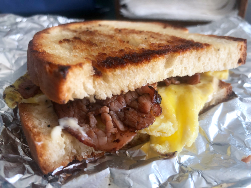 A ham, egg, and cheese sandwich from The Bread Company in Urbana is in a tin foil piece with the charred ham and peppery egg sticking out. Photo by Alyssa Buckley.