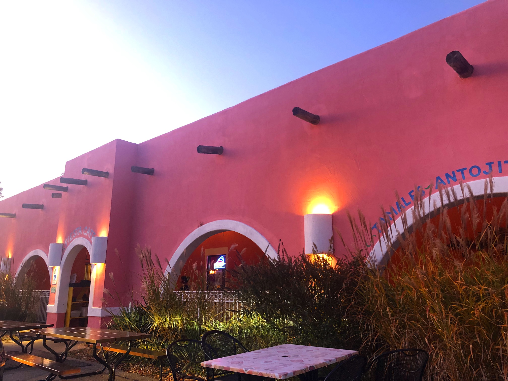 An outdoor photo of the exterior of Fiesta Cafe in Champaign, Illinois. The pink building has arched entryways and arched windows into the outdoor, covered patio. Photo by Alyssa Buckley.
