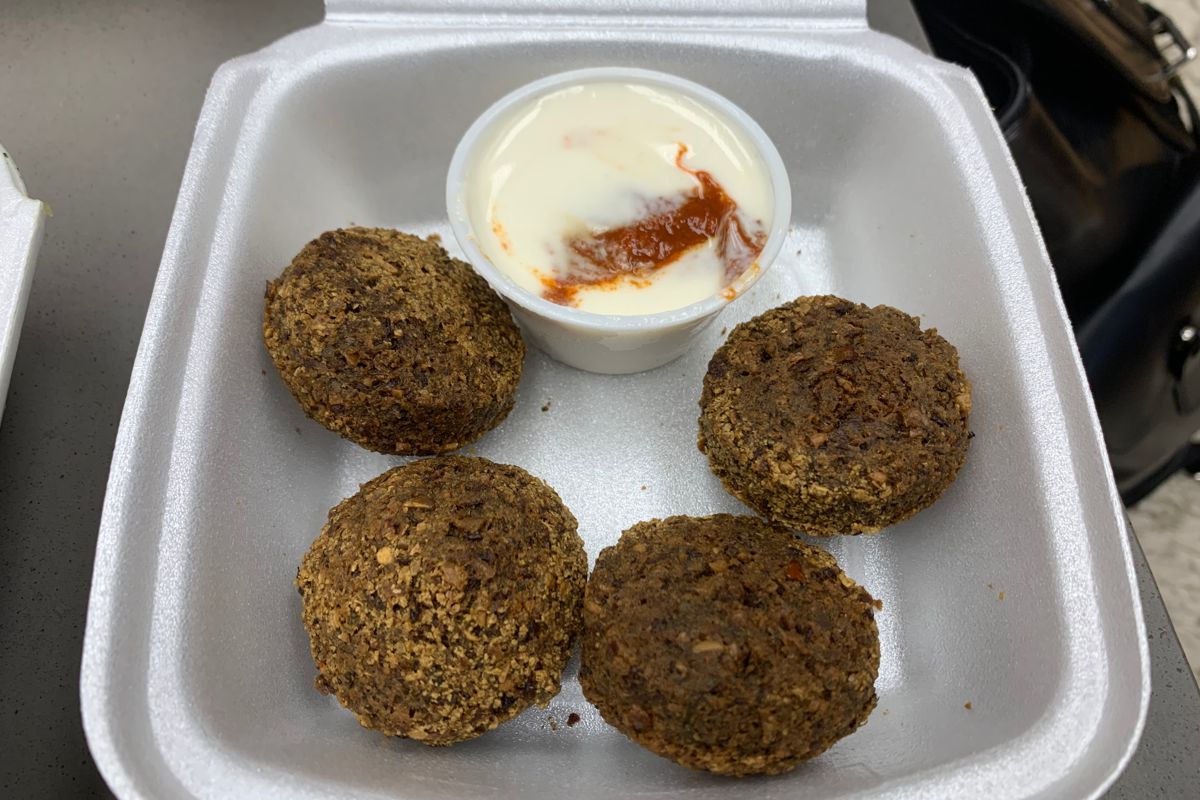 A small Styrofoam container with four fried falafel balls and a white tahini dip with red hot sauce mixed in. Photo by Megan Friend.