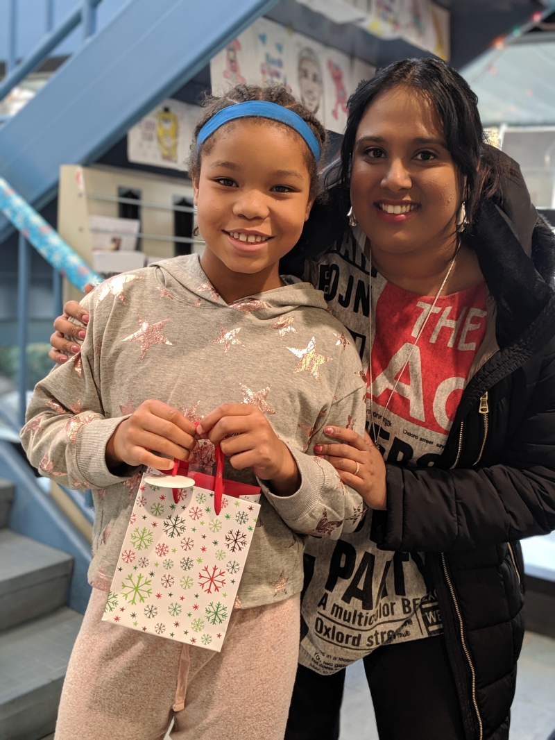 A woman has her arm around a preteen girl. They are both smiling. The girl is holding a gift bag with snowflakes on it. Photo provided by Aravinda Garimella.