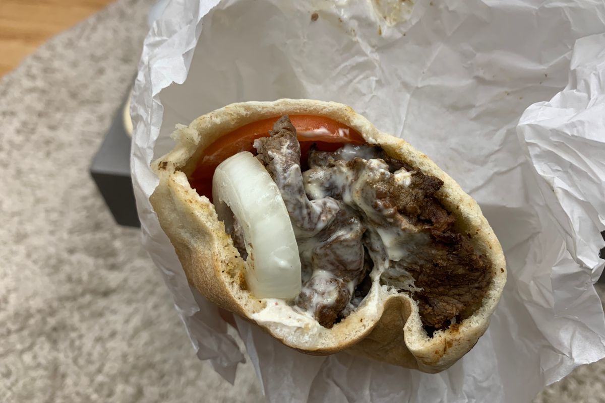 A photo taken from above of the beef gyro sandwich. The pita is open and filled with pieces of beef, a slice of onion and tomato and covered in a white sauce. Photo by Megan Friend.