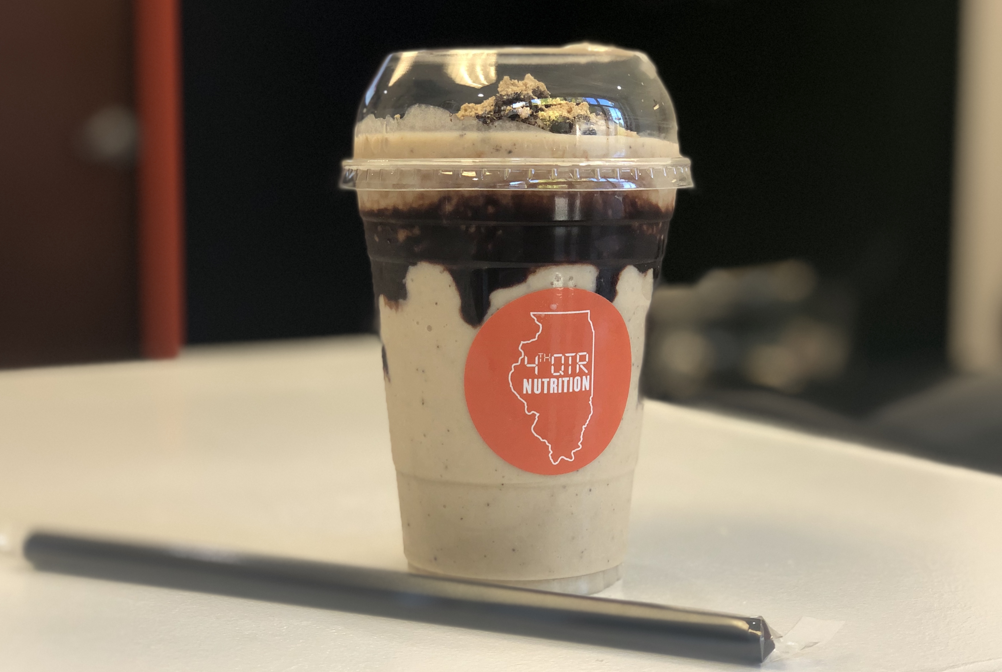 A light brown shake with drips of chocolate syrup in a plastic cup sits on a white counter with a black straw. Photo by Alyssa Buckley.