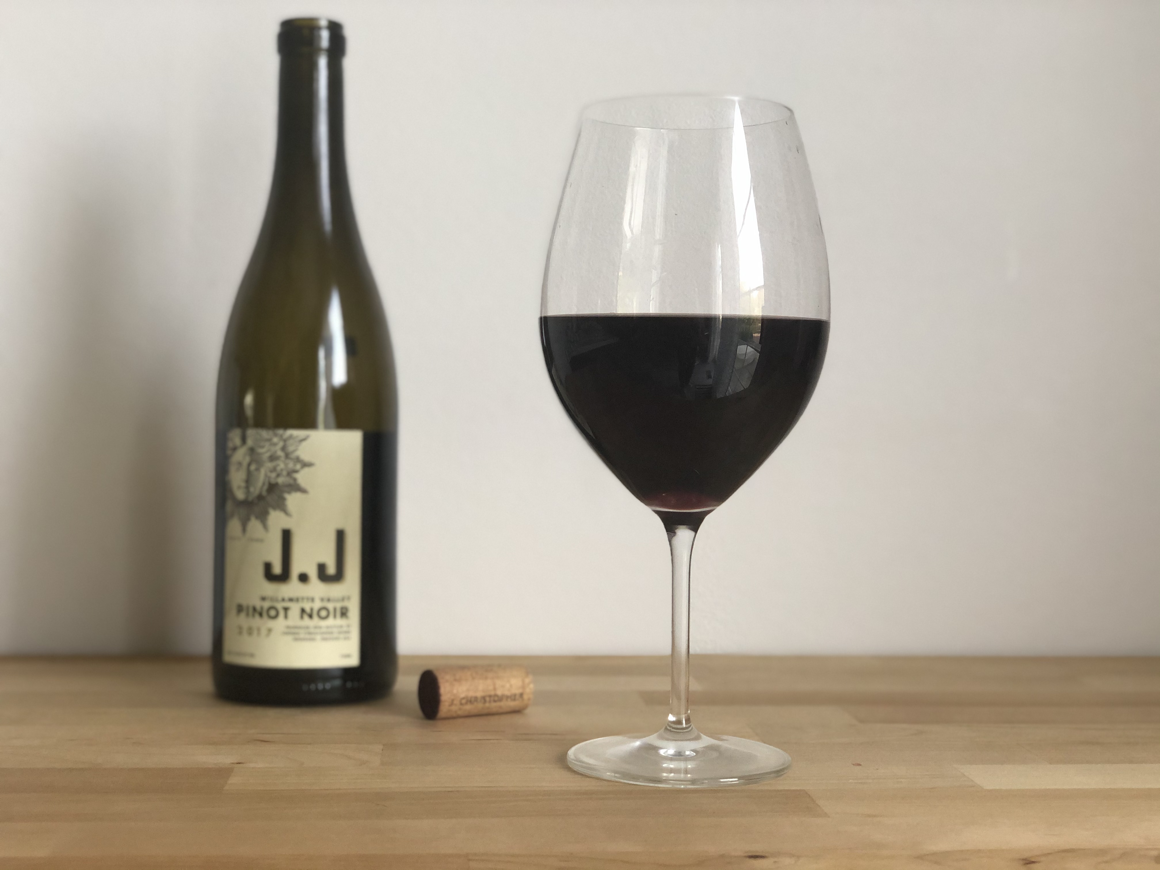 A glass of red is poured on a wooden counter with the bottle J.J. pinot noir with the cork. Photo by Alyssa Buckley.