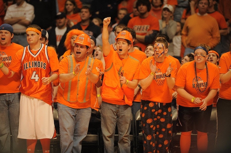 a group of illini fans clad in all orange cheer at a basketball game