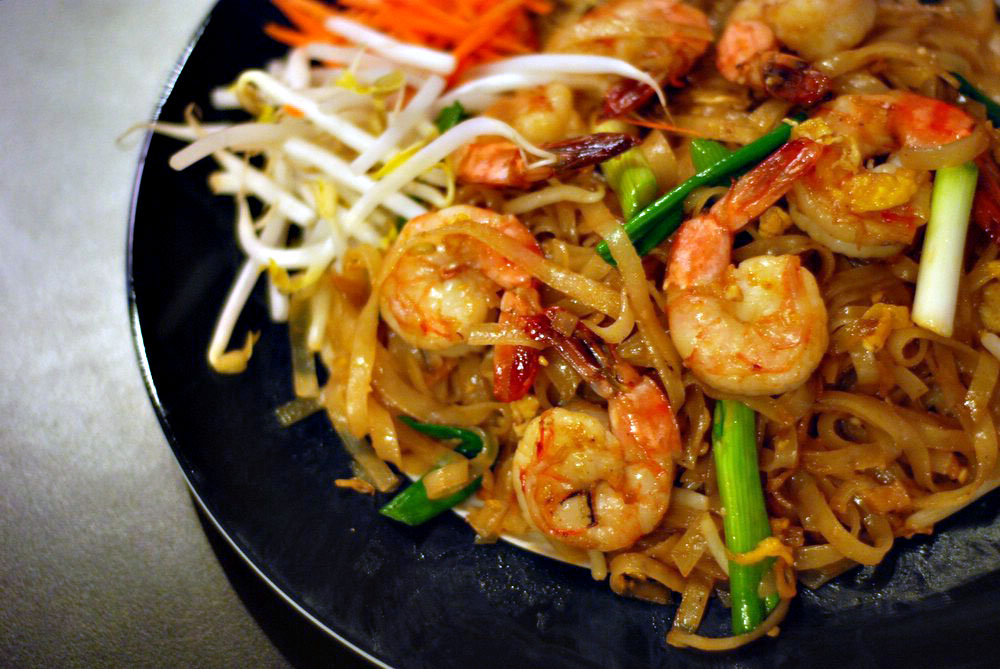 Shrimps dot the browned noodles while vegetables such as green onions and bean sprouts weave their way in between the spaces. Surrounding the main dish are ground peanuts, carrots, more bean sprouts, and a lime to add freshness to the fried elements. Photo by Siam Terrace.
