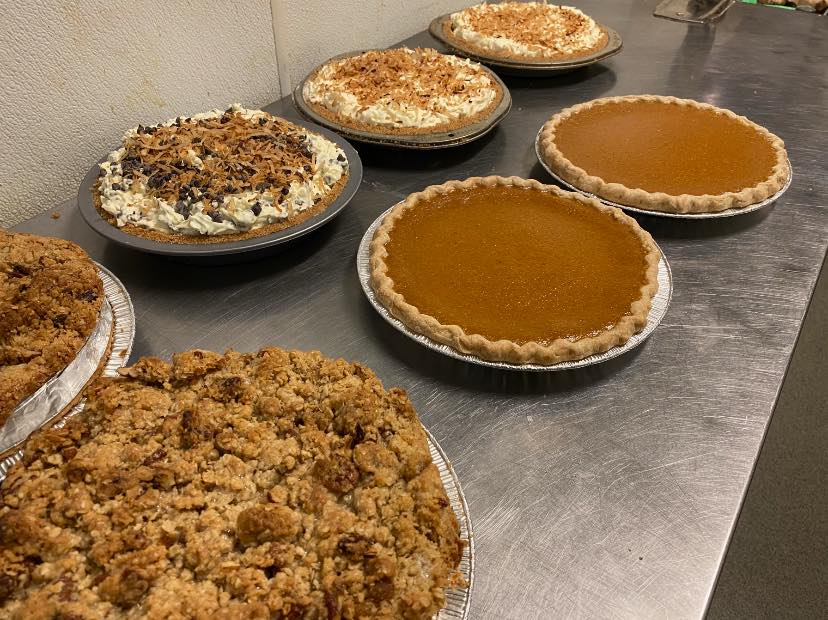 Several pies of varying toppings: crumble, whipped cream toppings, pumpkin, and coconut shaved toppings sit on a metal counter at Po' Boys in Urbana. Photo by Po' Boys Facebook page.