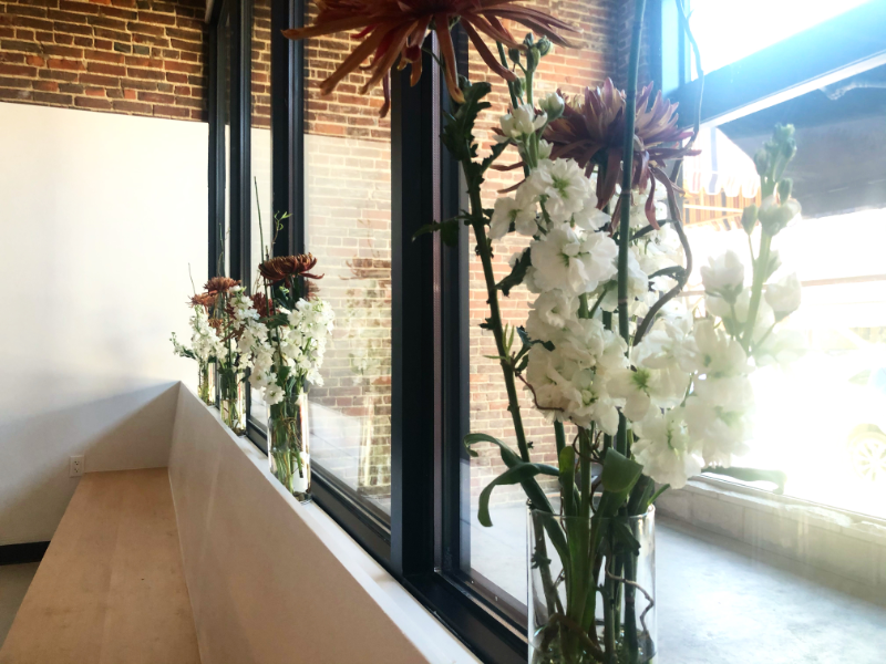 Several minimalist white bouquets are in glass bottles against the glass wall at the entrance of Suzu's Bakery in Downtown Champaign. Photo by Alyssa Buckley.