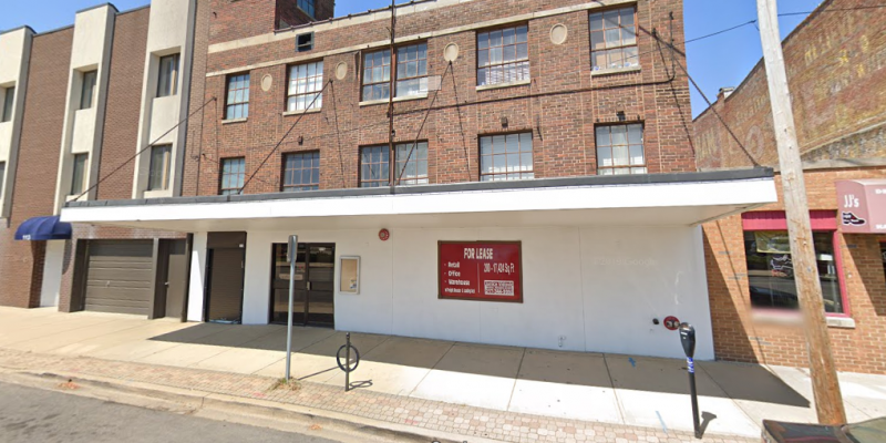 A building on a city street. The ground floor facade is white with a for lease sign on the wall. The rest of the three storey building is brick. Photo from Google Maps. 