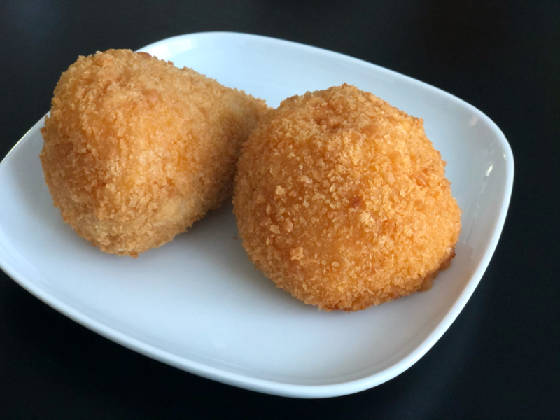 Two fried aracini balls from Nando Milano in Champaign sit on a white square plate on a black table. Photo by Alyssa Buckley.