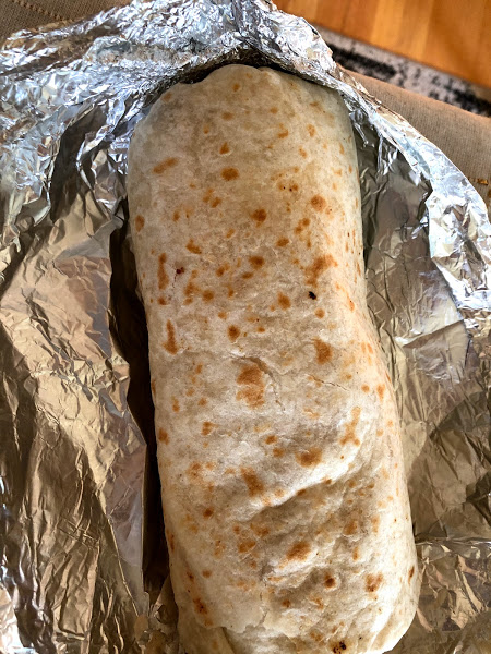A full burrito with light brown grill marks sits in tin foil. Photo by Remington Rock.