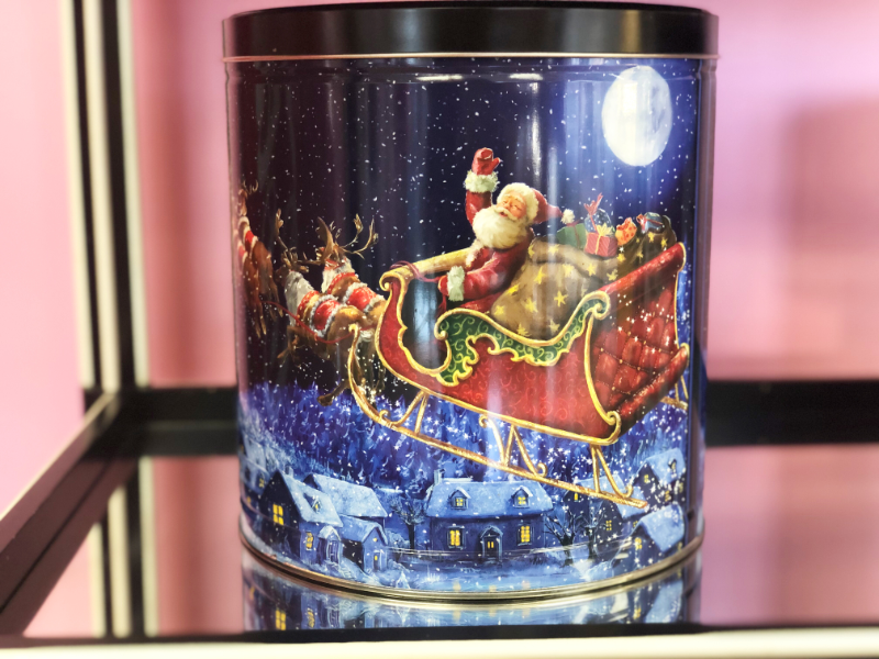 A holiday tin featuring Santa in his sleigh sits on a mirrored shelf in Cool Bliss Pop Bliss. Behind the tin, the wall is painted a pale pink. Photo by Alyssa Buckley.