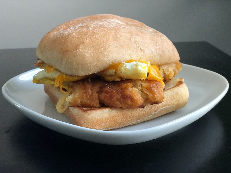A single morning bender sandwich from Cracked! The Egg Came First sits on a white plate. The sandwich has egg, hashbrowns, cheese, and cream cheese inside the soft bun. Photo by Alyssa Buckley.