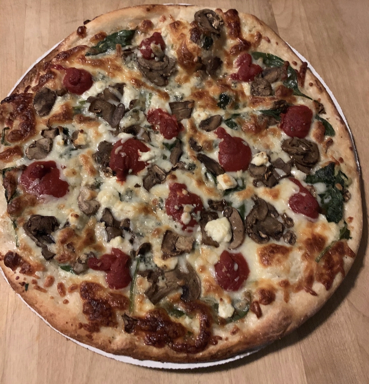 a freshly baked pizza with goat cheese, mushrooms, basil and heavy amounts of tomato sauce 