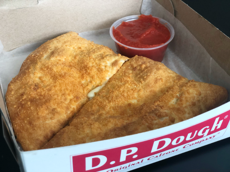 A calzone with a parmesan crust is sliced in half inside a DP Dough box with parchment paper and a cup of marinara sauce. Photo by Alyssa Buckley.
