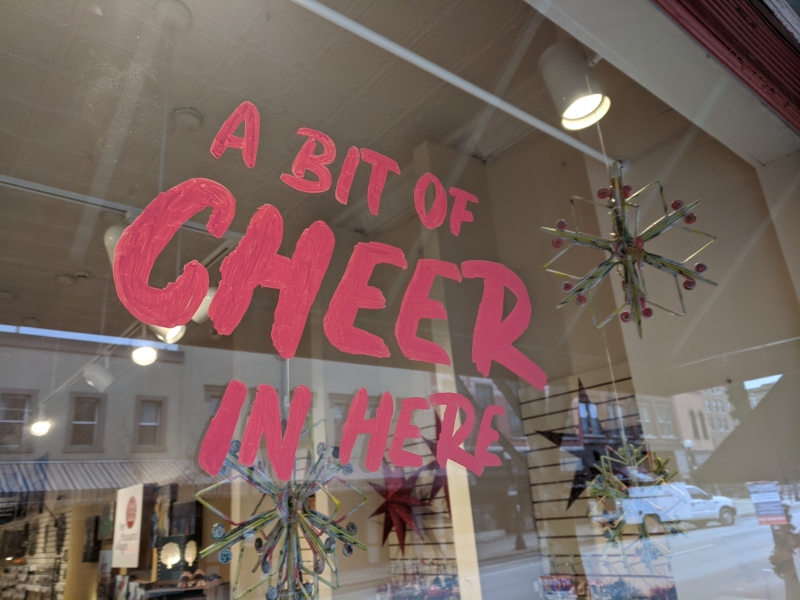 A store window is painted with a message in red block letters: A bit of cheer in here. Photo by Tom Ackerman.
