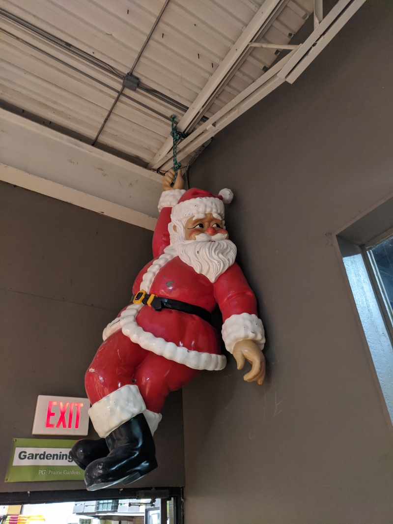 A life sized Santa decoration is hanging from the ceiling. The figure is looking to the side, and the other arm is dangling at it's side. Photo by Tom Ackerman.