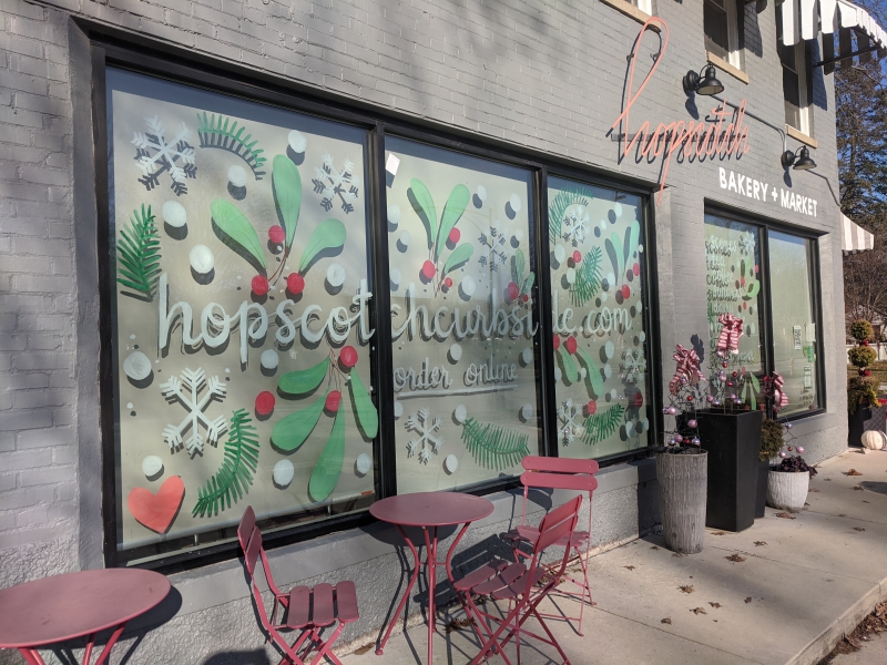 The windows of Hopscotch Bakery and Cafe are painted with holly, hearts, snowflakes, pine branches, and polka dots. Along the windows there are small tables and chairs. Photo by Tom Ackerman.