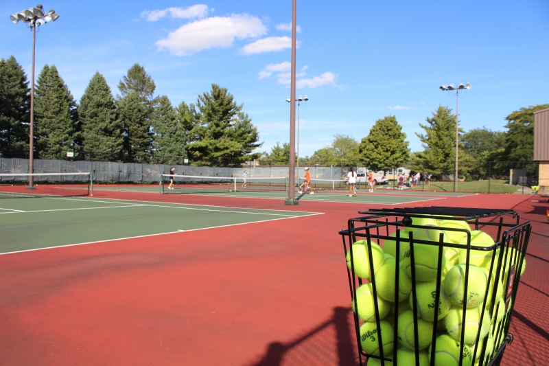 people playing tennis on courts with a bucket of balls in the foreground
