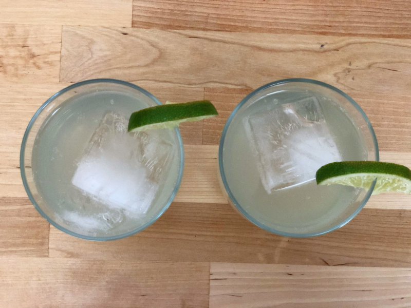 An overhead shot of two cocktails on a butcher block counter. The drinks are in half tumblers with a lime wedge on the side. Photo by Alyssa Buckley.