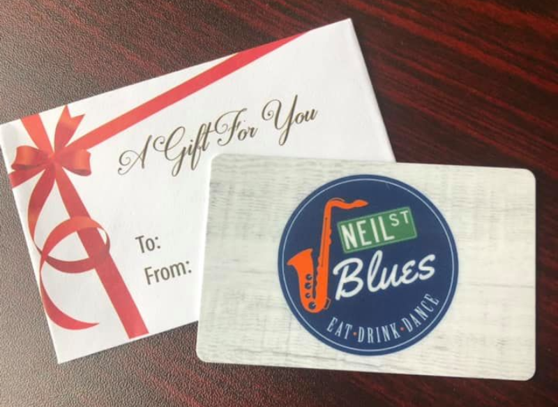 A gift card to Neil St. Blues sits on a dark wood table with a white envelope reading in cursive 