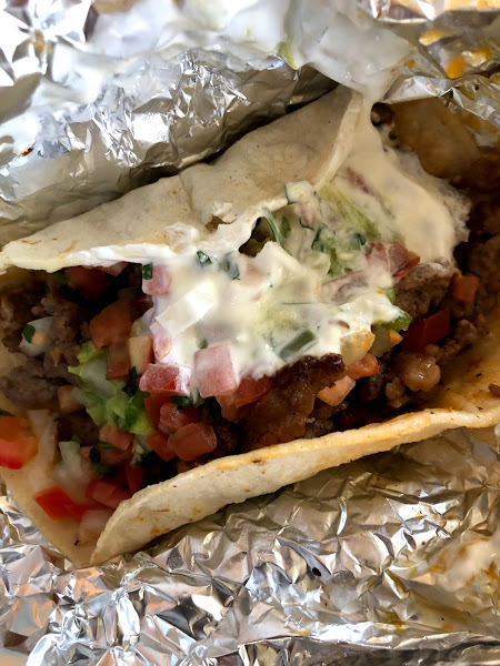 A steak taco sits in a tin foil wrapper. The taco is covered in salsa and sour cream. Photo by Remington Rock.