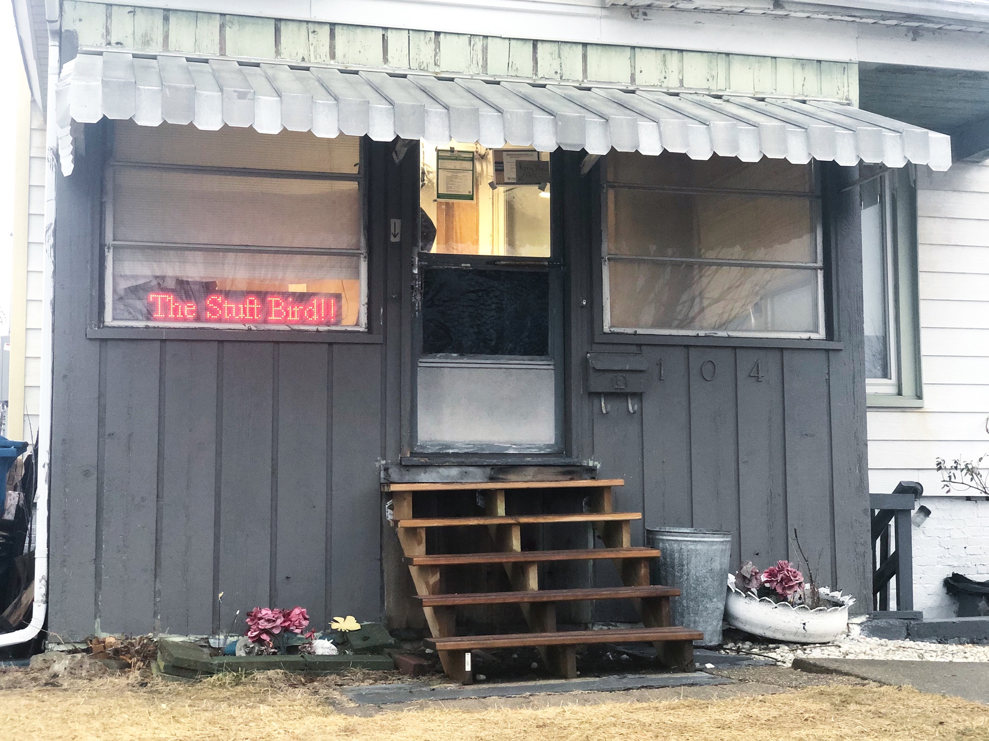 An exterior photo of The Stuft Bird's pickup porch which is dark blue-gray with wooden steps and planted colorful flowers. Photo by Alyssa Buckley.