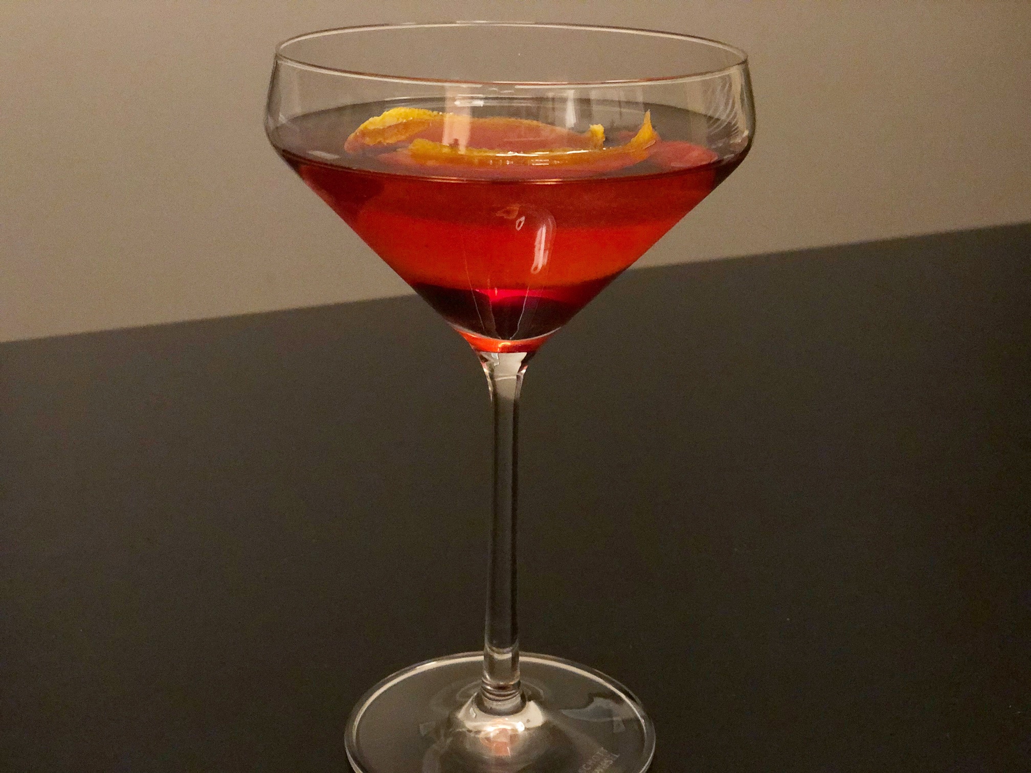 In a tall cocktail glass, a ruby red cocktail has a lemon peel garnish and a cherry at the bottom. Photo by Alyssa Buckley.