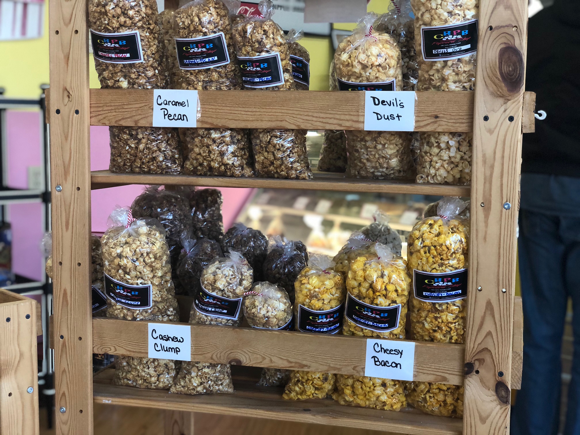 A wooden shelf holds several bags of popcorn in the Cool Bliss Pop Bliss popcorn shop on Neil Street in Champaign. Photo by Alyssa Buckley.