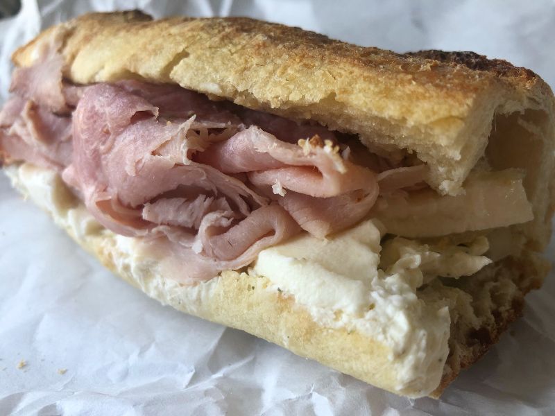 A side view of Frankensandwich from Cheese & Crackers. Pink ham is overflowing from the sandwich which rectangular chunks of Mozzarella underneath and a white spread on the bottom of the bread. Photo by Alyssa Buckley. 
