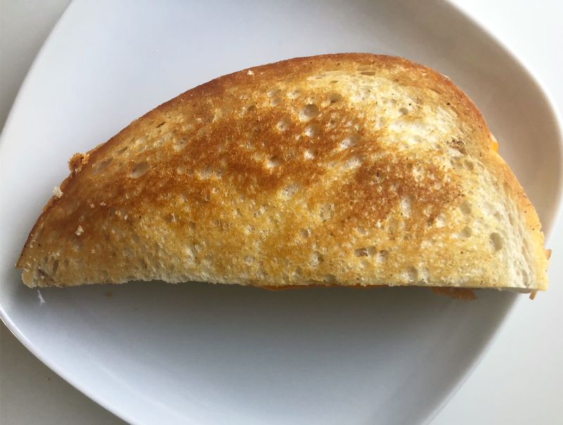 A golden brown half sandwich, sliced on a diagonal, sits on a white plate on a white table. Photo by Alyssa Buckley.