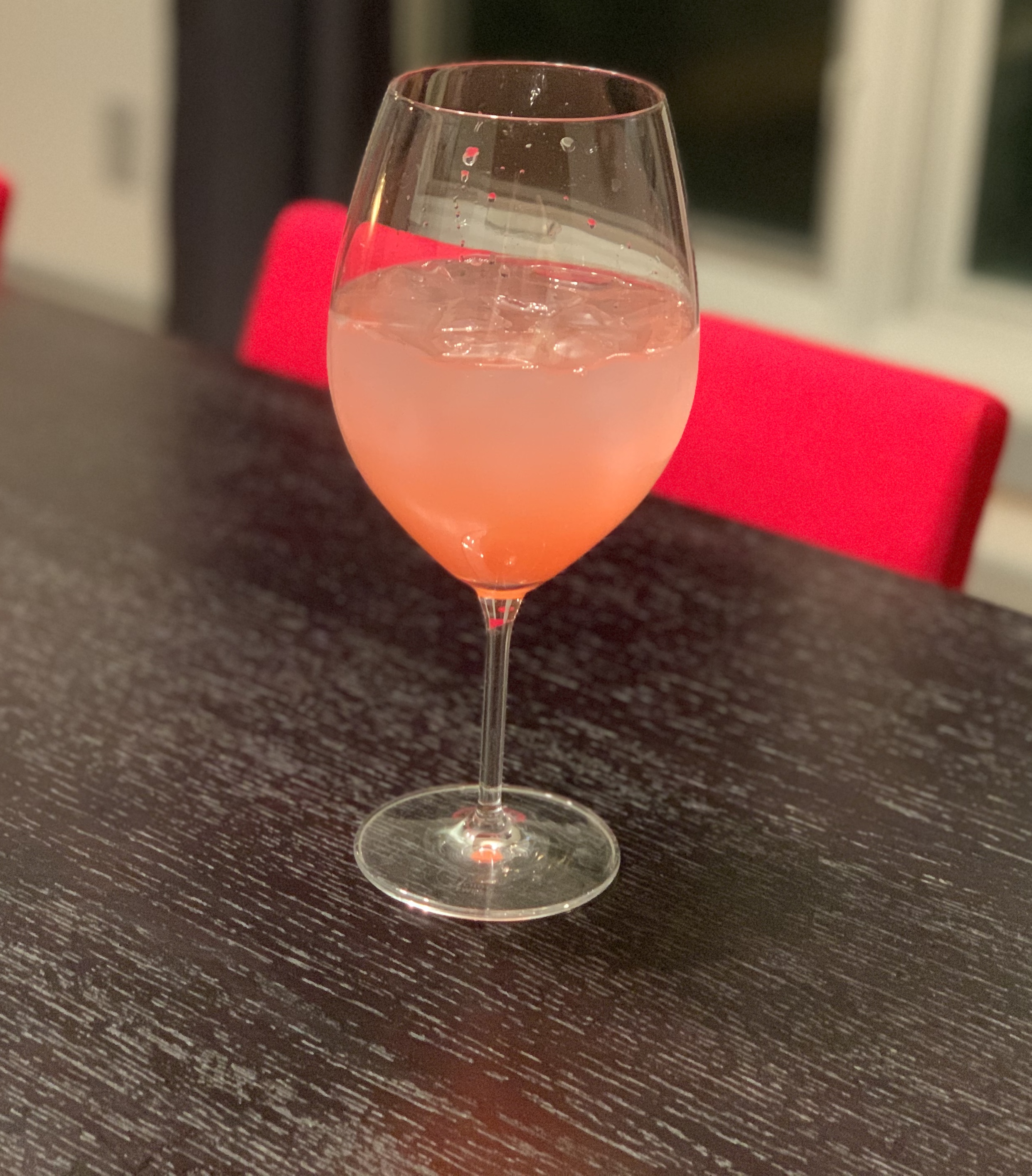 In a stemmed wine glass, there is a pink cocktail. The glass is on a black, wood-grained table. Photo by Stephanie Wheatley.