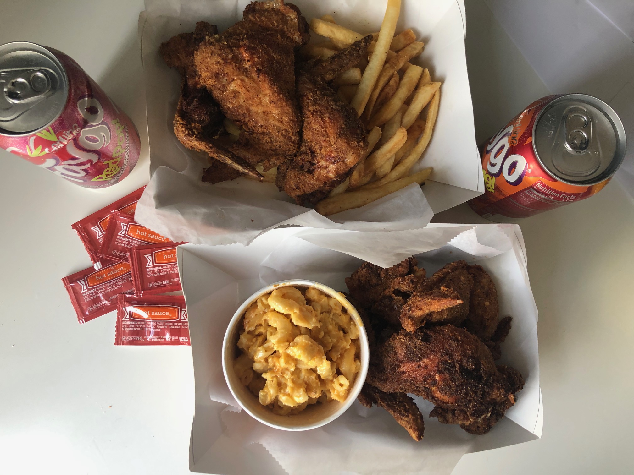 An overhead photo of two meals from The Stuft Bird. One carryout box contains three wings with a cup of macaroni, and the bottom contained three wings with fries. Two cans of Faygo soda sit beside the meals. Photo by Alyssa Buckley.