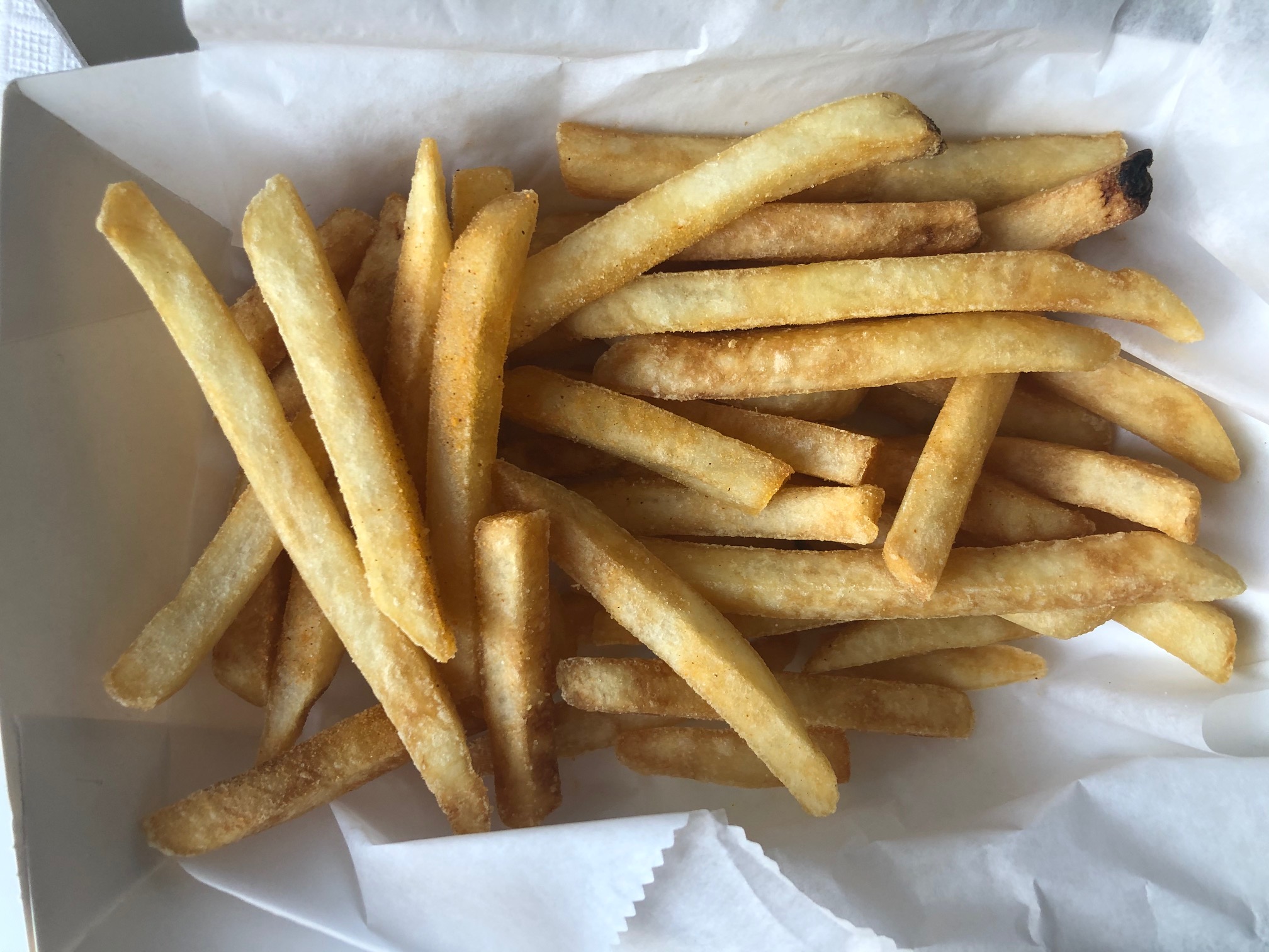A white carryout box contains a medium sized portion of straight fries dusted with seasoning. Photo by Alyssa Buckley.