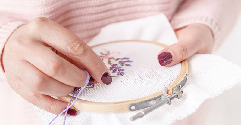 Close up of woman's hands working on cross-stitch embroidery. Photo from the Urbana Free Library Facebook page