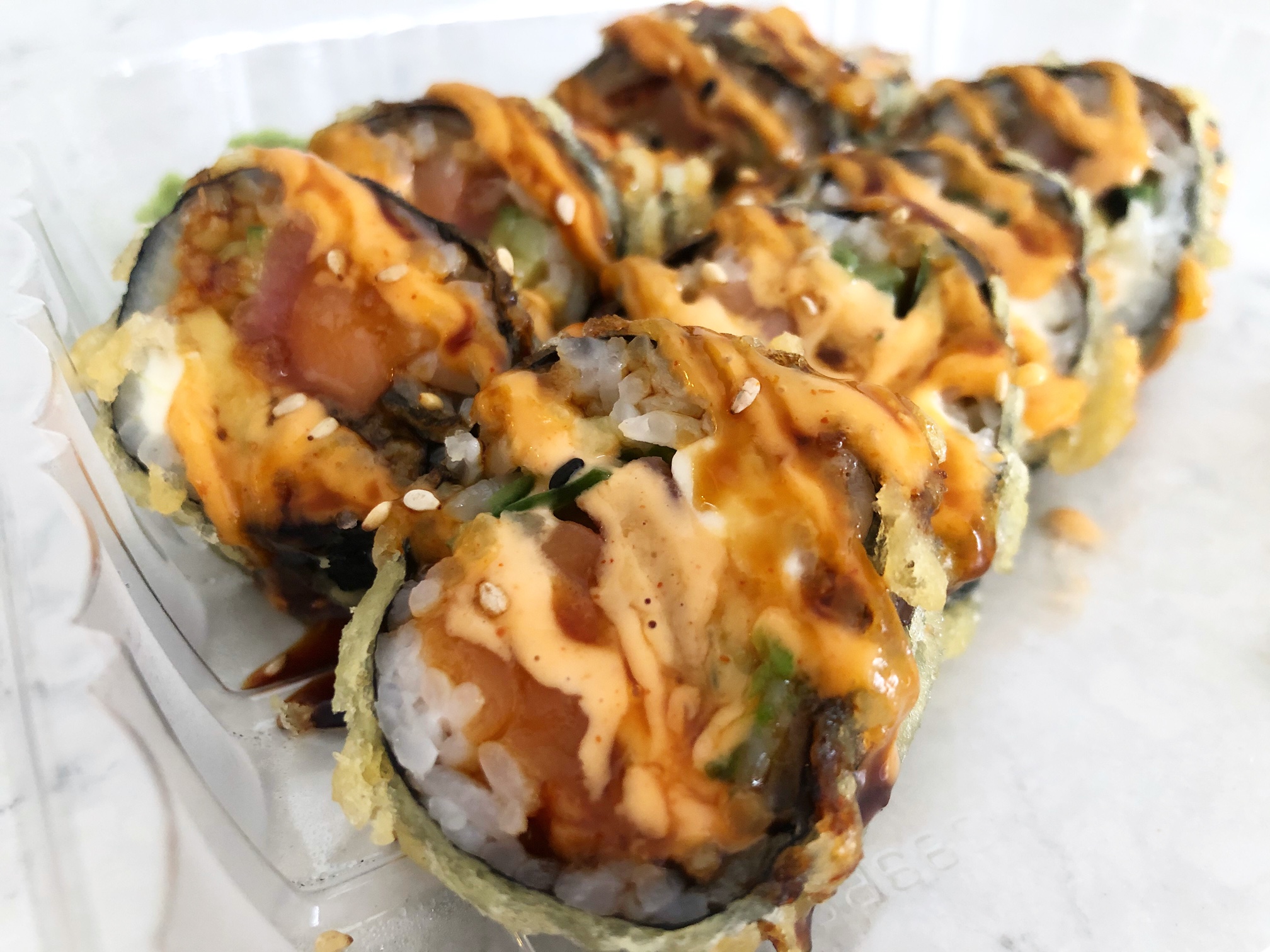 A large sushi roll cut into ten pieces has been deep fried with a light brown tempura batter with two sauces drizzled on top: orange spicy mayo and a dark brown eel sauce. Photo by Alyssa Buckley.