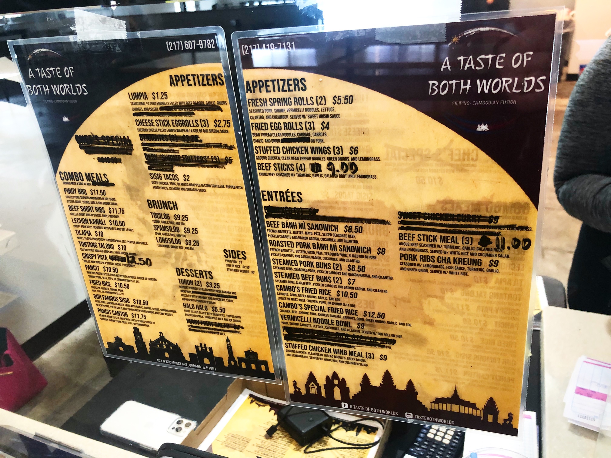 Two menus are posted at A Taste of Both Worlds on the plexi glass at the restaurant. Some of the menu items are crossed out with Sharpie. Photo by Alyssa Buckley.