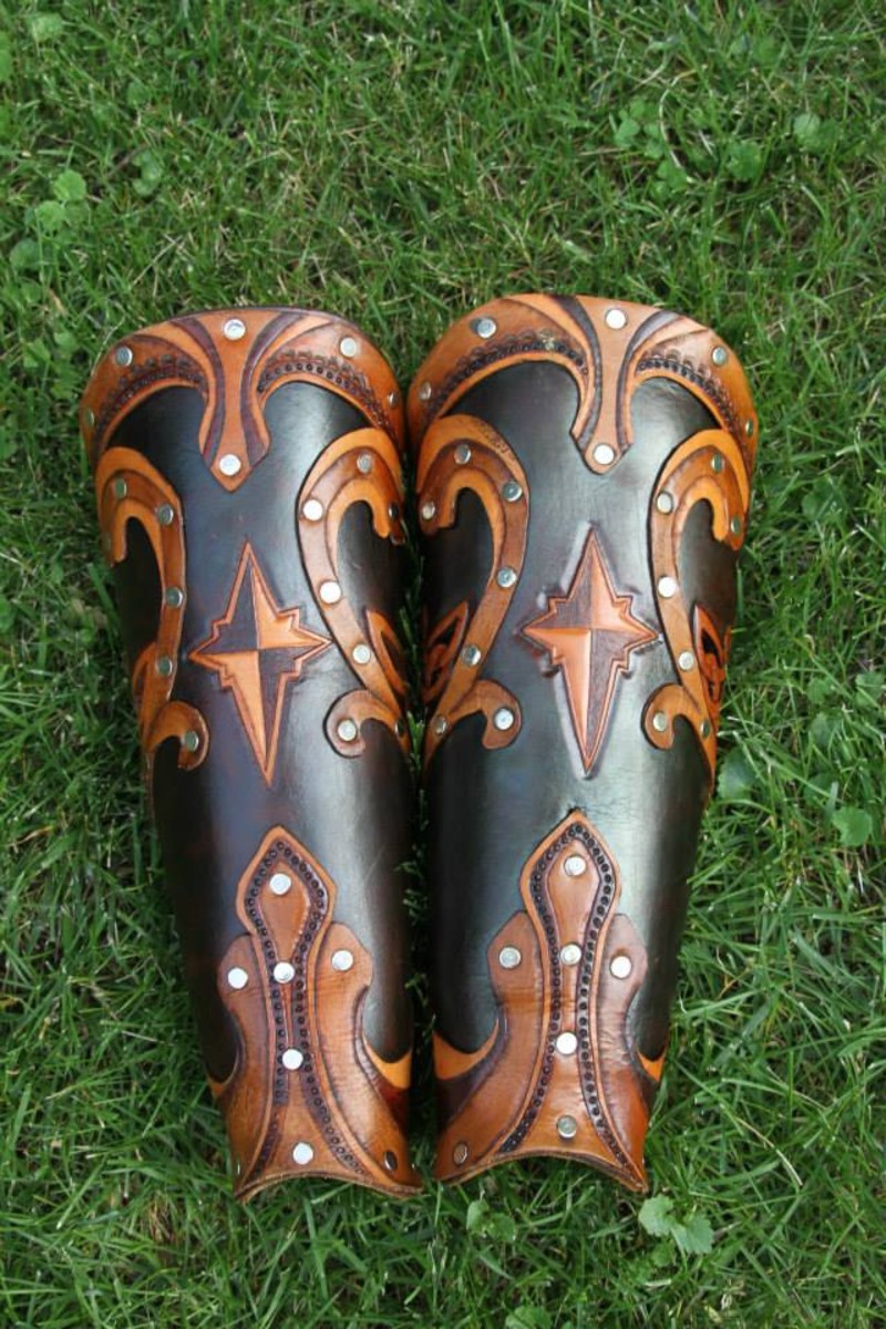 Two intricately patterned leather bracers sit side-by-side in the grass. Photo by Brittany Norman.