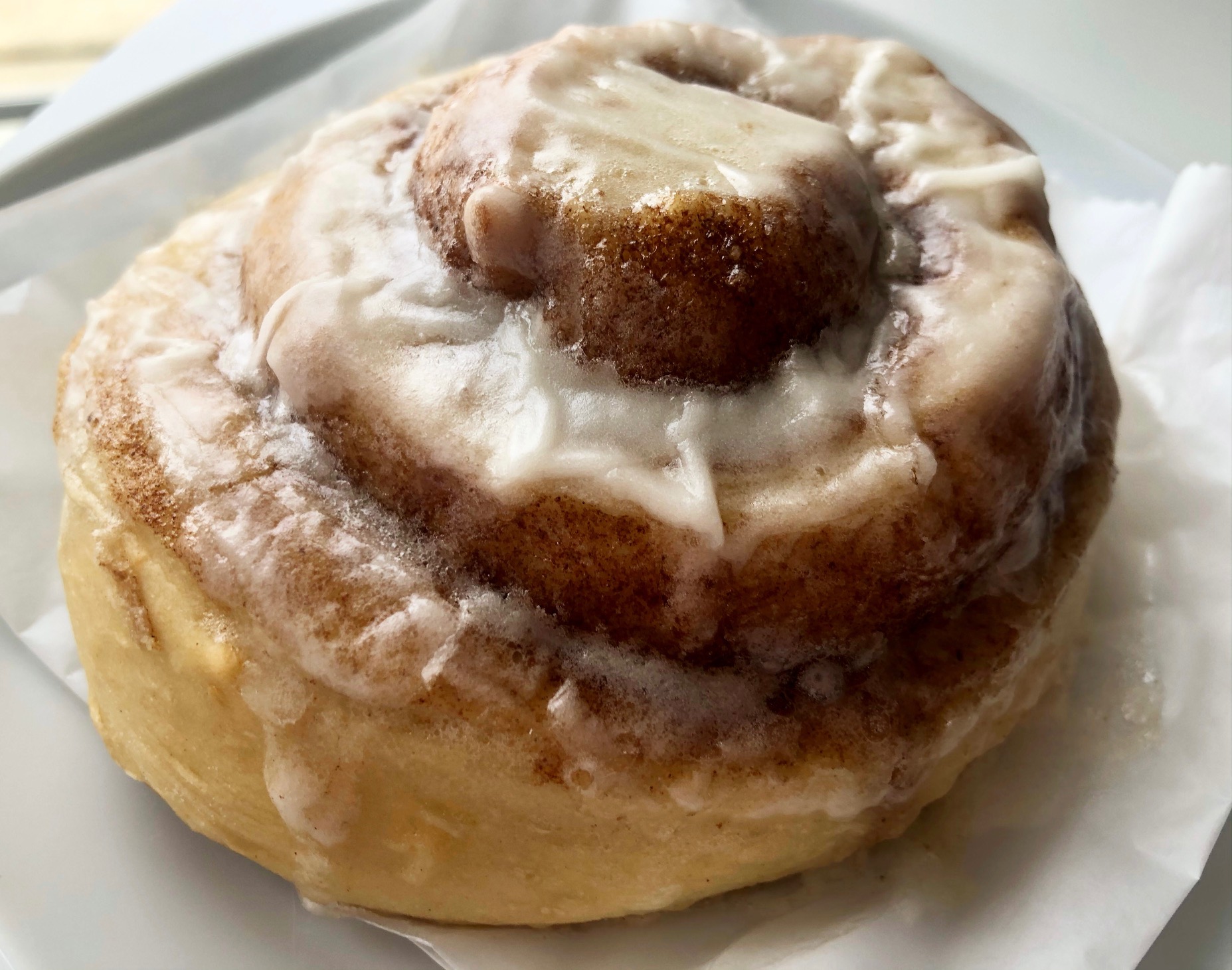 A giant cinnamon roll sits on a white plate on a white table. The cinnamon is swirled like a tower, and the icing is cracking. Photo by Alyssa Buckley.