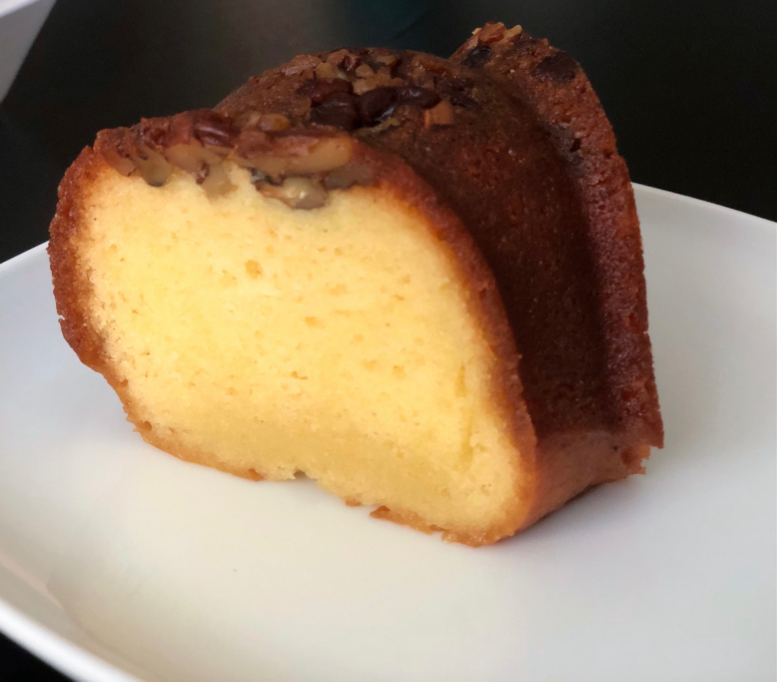A slice of yellow rum cake from Caribbean Grill is on a white plate. The cake is a rich yellow throughout and a dark brown exterior with chopped nuts on top. Photo by Alyssa Buckley.