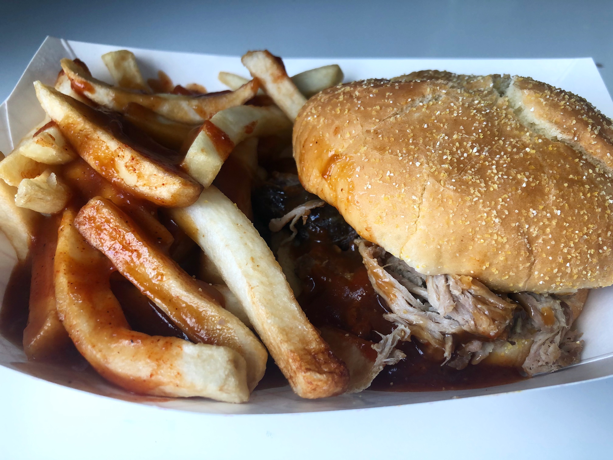 In a small paper tray, there are fries covered in barbeque sauce beside pulled pork sandwich from Wood N Hog. Photo by Alyssa Buckley.