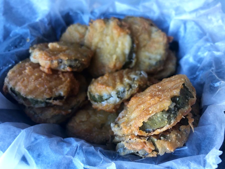 Fried pickles in a takeout container on parchment paper are golden brown with a bit of the dark green skin of the pickle poking through the thin batter. Photo by Alyssa Buckley.