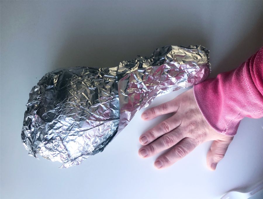 A tin foil wrapped turkey leg sits on a white table with the author's white hand in a pink long sleeved shirt is next to it, and less than half the size. Photo by Alyssa Buckley.