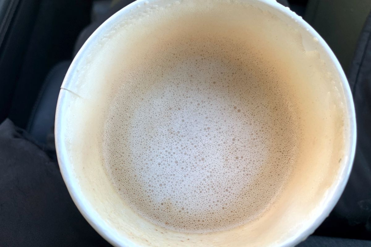 A photo looking down into a to-go coffee cup. It shows a slightly foamy, light brown coffee drink from Hopscotch. Photo by Megan Friend.