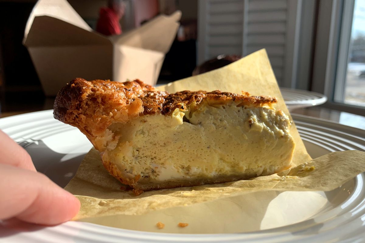 A side view photo showing a slice of egg quiche. The top is brown with melted cheese and egg and the side shows a soft, pillow-like egg center. The slice has an edge like that of a pie. Photo by Megan Friend.