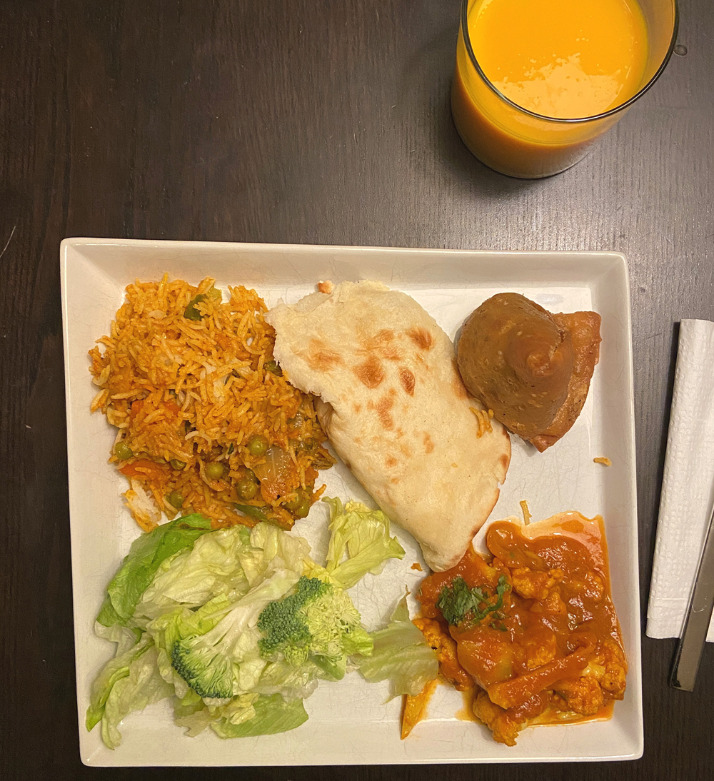 A plate of food from Kohinoor. Clockwise, from top left: vegetable biryani, naan, samosa, aloo gobi, green salad. A glass of mango lassi sits on the table above the plate. Photo by Jessica Hammie. 