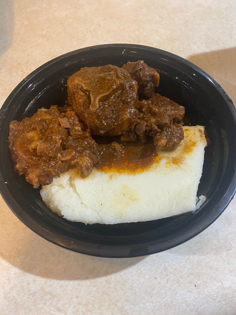 Oxtails covered in brown gravy and a creamy white nshima are in a round black plastic container. Photo by Julie McClure.