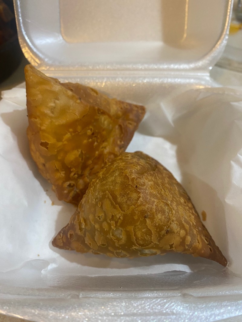 There are two triangle shaped golden brown samosas are in a white Styrofoam container. Photo by Julie McClure.