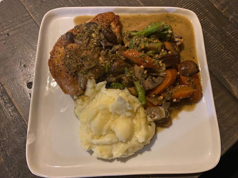 A square white ceramic plate has a chicken breast is flanked by a dollop of mashed potatoes and mixture of carrots, broccoli, and mushrooms. It is all covered in a light brown sauce. Photo by Julie McClure.