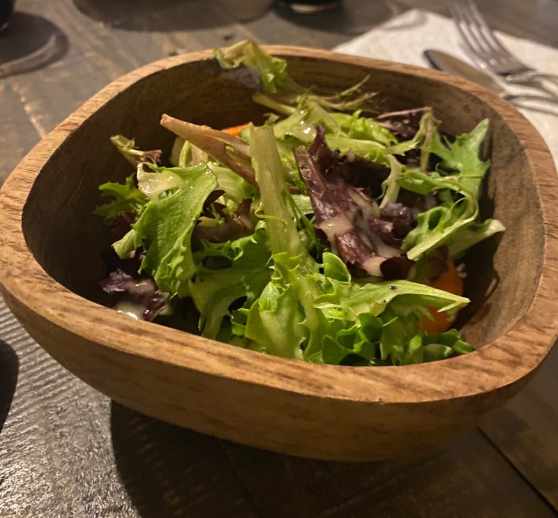 A wooden bowl is filled with mixed greens covered in a slightly creamy vinaigrette. Photo by Julie McClure.